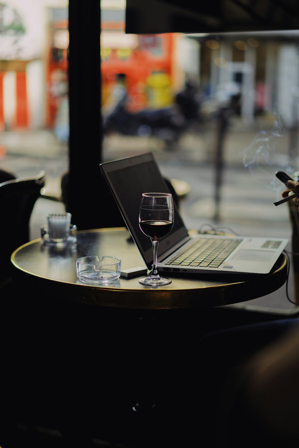 Hand holds a cigarette and smartphone near a cafe table.