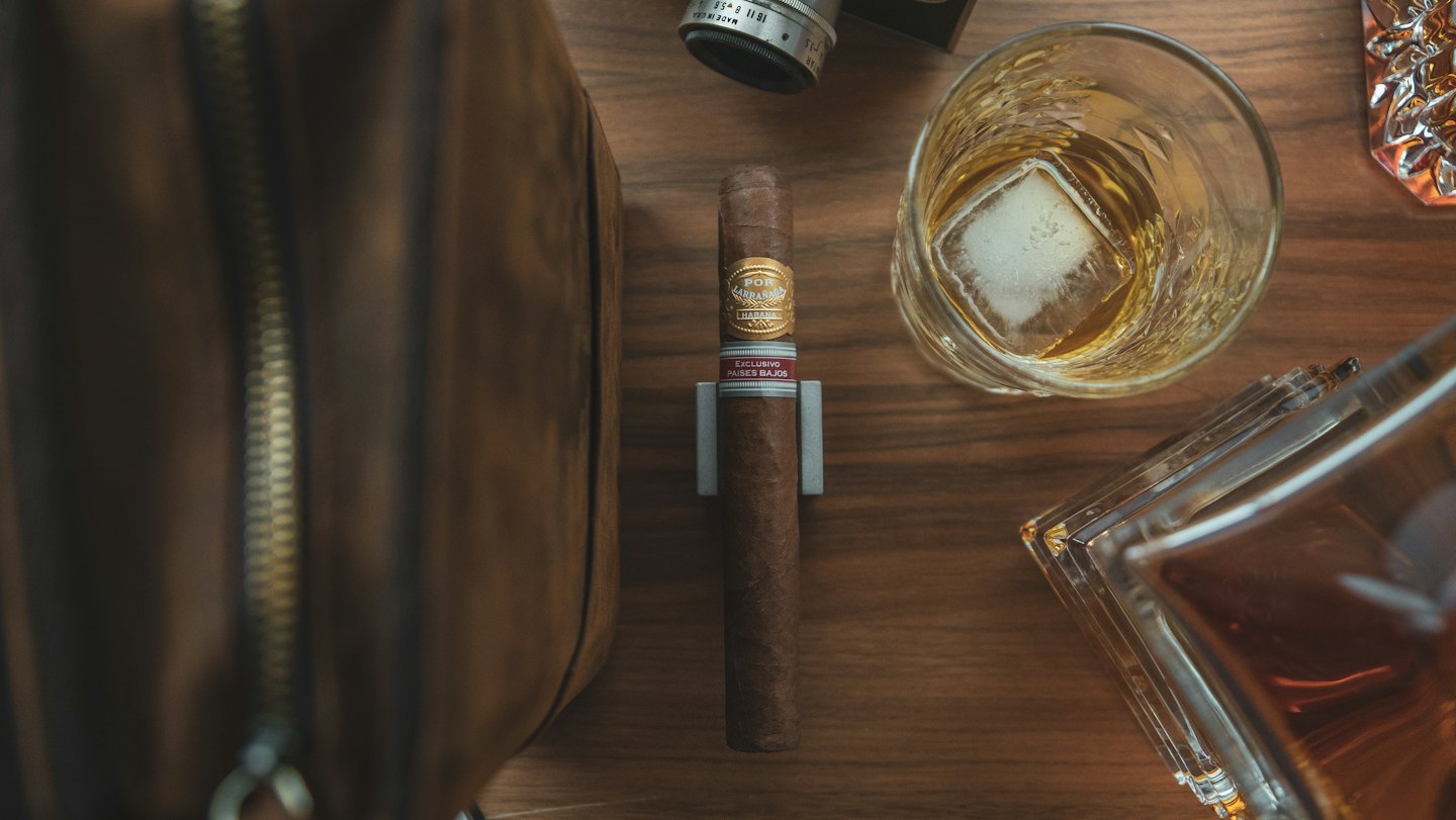 Cigar, whiskey, and vintage camera lens on a wooden table.